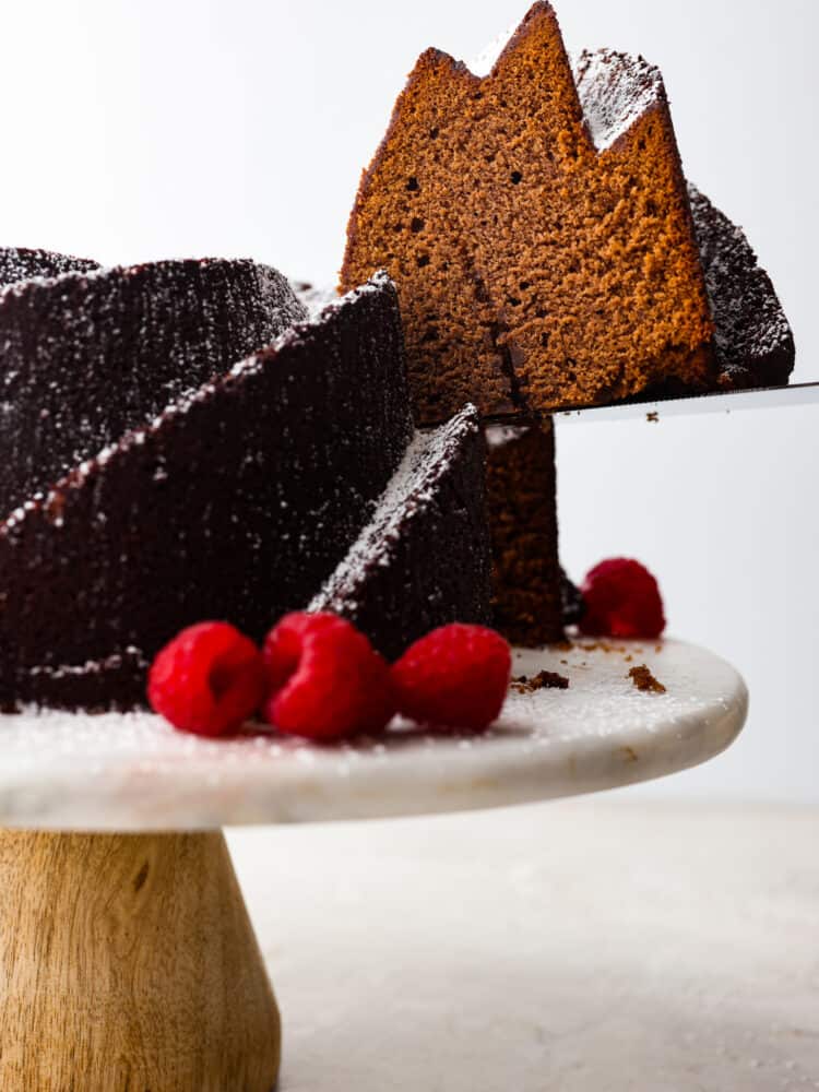 Get ready to eat the best dessert that you will have all year long! This chocolate pound cake tastes as good as it looks, and it is the perfect dessert for any occasion! The side view of a chocolate pound cake on a cake stand with a slice being taken out.