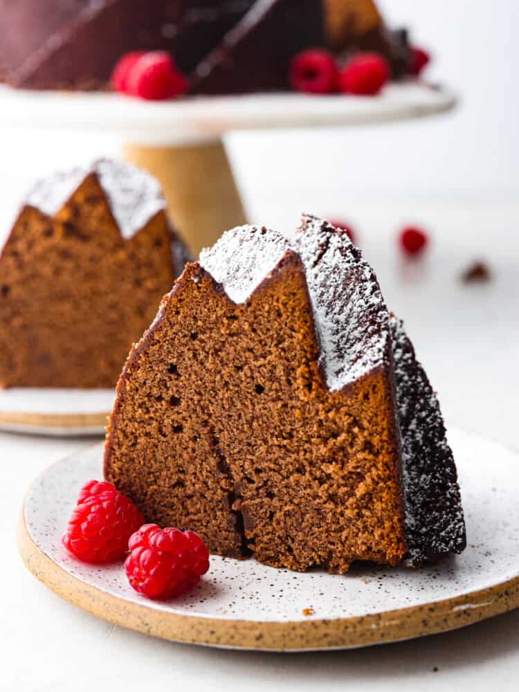 Get ready to eat the best dessert that you will have all year long! This chocolate pound cake tastes as good as it looks, and it is the perfect dessert for any occasion! A slice of chocolate pound cake with some raspberries next to it, on a plate.