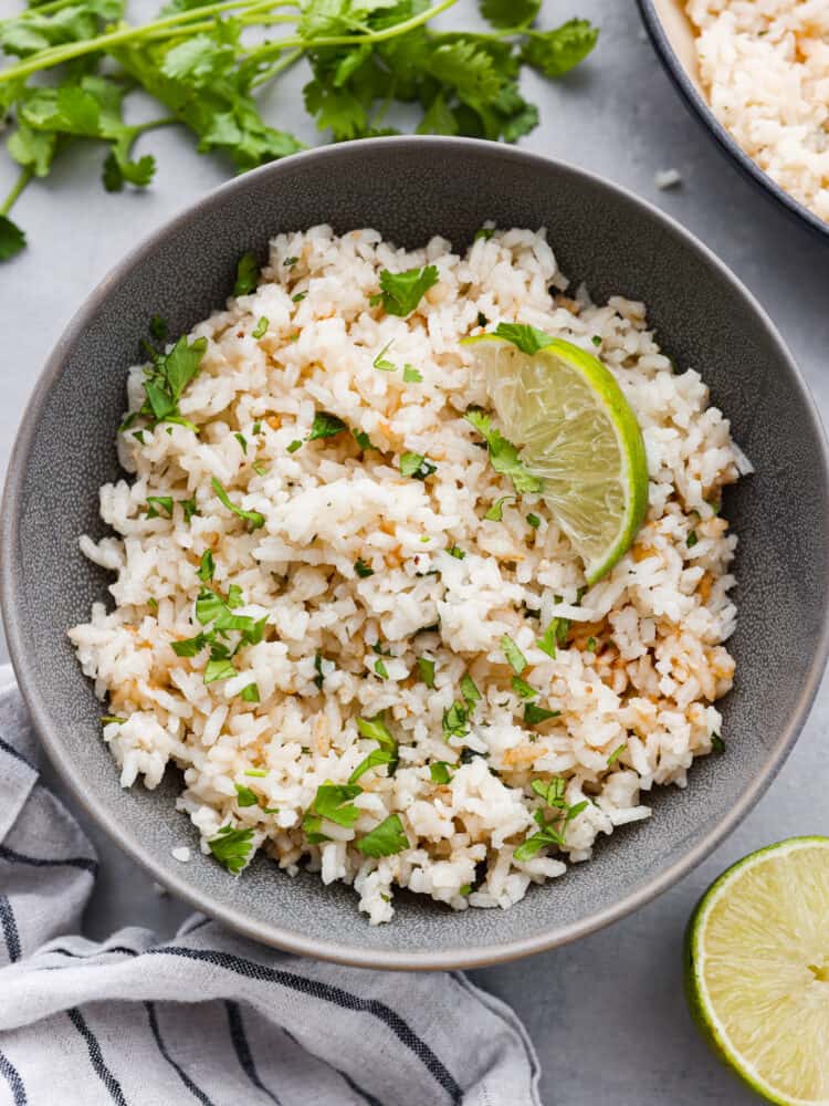 This cilantro lime rice makes the perfect side dish to complement any Mexican meal! It is packed with flavor, and the best part is... it takes less than 30 minutes to make! A gray bowl of cilantro lime rice with a lime wedge on top.
