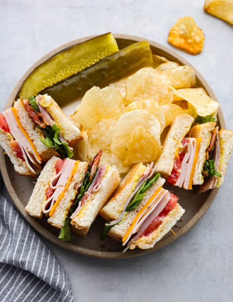 There’s a reason why club sandwiches are so popular - you can’t go wrong with 3 pieces of toasty bread smothered in mayonnaise, mustard, and then layered with meat, cheese, and fresh greens! This classic club sandwich recipe is going to be your new lunch go-to. 4 club sandwiches served alongside pickles and potato chips.