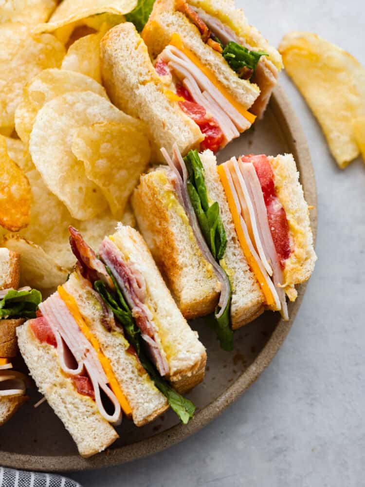 There’s a reason why club sandwiches are so popular - you can’t go wrong with 3 pieces of toasty bread smothered in mayonnaise, mustard, and then layered with meat, cheese, and fresh greens! This classic club sandwich recipe is going to be your new lunch go-to. 3 club sandwiches served on a plate with potato chips.