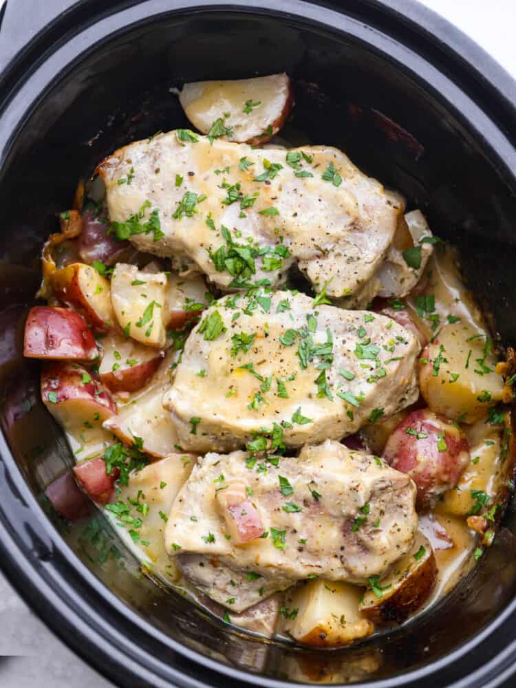 Weeknight magic in one pot! These slow cooker ranch pork chops are rich, comforting, and packed with flavor. With just a few ingredients, you’ll have tender pork and perfectly cooked potatoes swimming in a creamy ranch sauce. Cooked pork chops and potatoes covered in a creamy, golden sauce garnished with parsley in the base of a slow cooker.