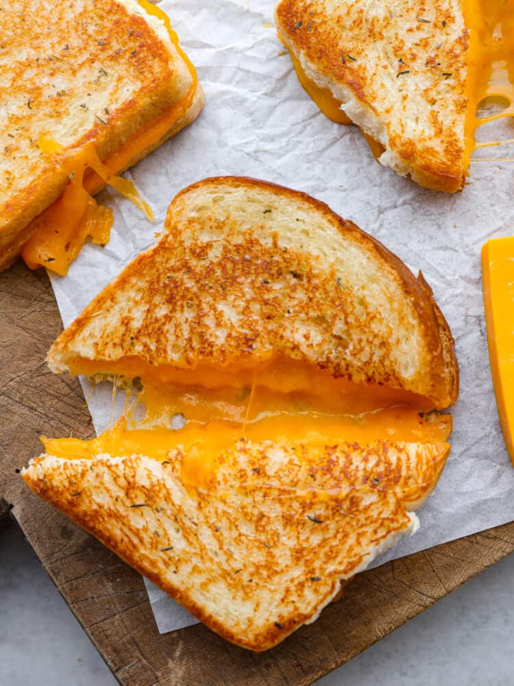 You will never cook another grilled cheese sandwich again after you try this one! It's deliciously cheesy on the inside, and once you sink your teeth into that crispy outside, it is absolute perfection! A grilled cheese sandwich on parchment paper, cut on the diagonal and pulled apart about an inch so that you can see the melted cheese inside.