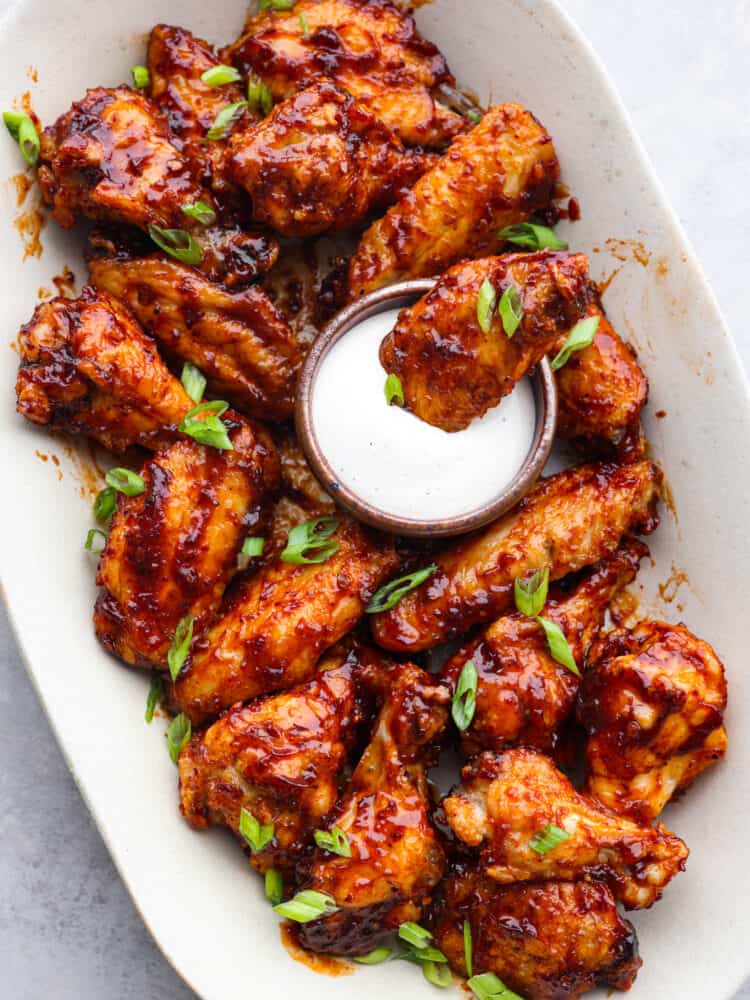 Honey chipotle wings are sweet and spicy and pack a punch of flavor! You will definitely want to serve them as an appetizer on any game day, and they will be the hit of the party! A platter of wings with one being dipped into ranch dressing.