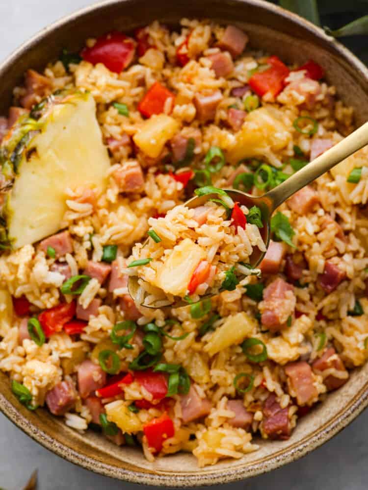 This Hawaiian fried rice is loaded with sweet pineapple, ham, and veggies and is so much better than takeout! Everyone goes crazy over this meal, and it's definitely a family favorite! A close up of a spoonful of Hawaiian fried rice with a bowl of fried rice blurred in the background.