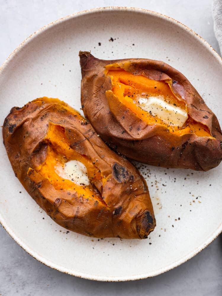 Using an Instant Pot to cook your sweet potatoes is the best! They turn out perfectly sweet, creamy, and soft in half the time it takes to bake them! 2 fully cooked sweet potatoes sliced open and served with butter and salt and pepper.