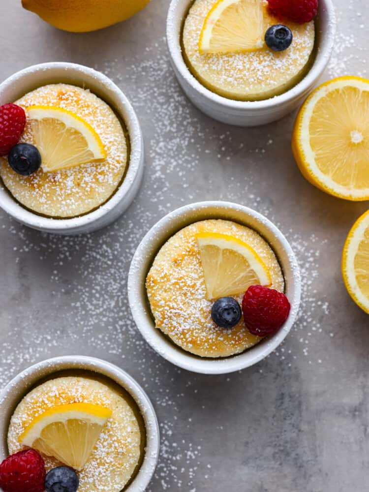 This lemon pudding cake is gorgeous, decadent, and delicious! Dusted with powdered sugar and topped with fresh berries, it's perfect for impressing your guests on any occasion! The top view of lemon pudding cake in 3 ramekins. Each dusted with powdered sugar and topped with berries.