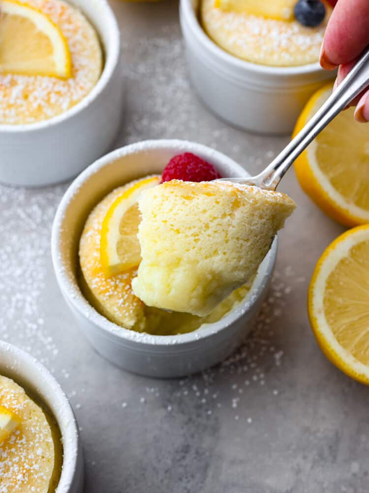 This lemon pudding cake is gorgeous, decadent, and delicious! Dusted with powdered sugar and topped with fresh berries, it's perfect for impressing your guests on any occasion! lemon pudding cake being scooped out with a spoon.