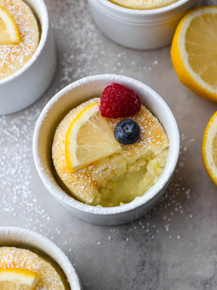 This lemon pudding cake is gorgeous, decadent, and delicious! Dusted with powdered sugar and topped with fresh berries, it's perfect for impressing your guests on any occasion! Lemon pudding cake in a ramekin with a bite taken out of it.