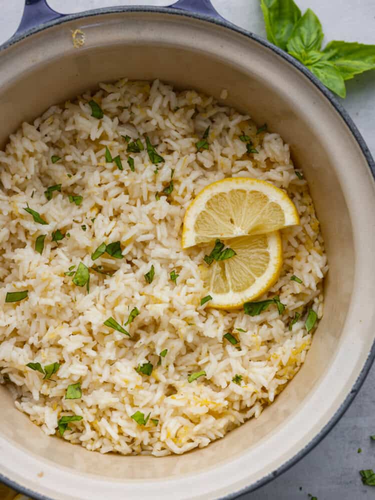 This zesty lemon rice is the perfect summer side dish! It's creamy, savory, and packed with bright citrus flavor! Serve it with your favorite fish or meat dishes for a crave-worthy meal. Lemon rice in a blue pot, garnished with lemon and herbs.