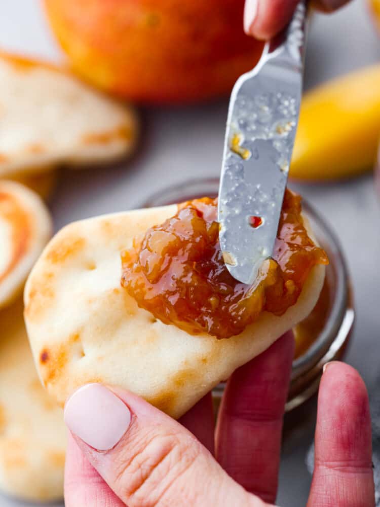 This delightful mango chutney is a spread that can be used in so many different recipes! It packs a punch when it comes to flavor, and you will always want to have some on hand! A knife spreading some mango chutney on a small piece of naan bread.