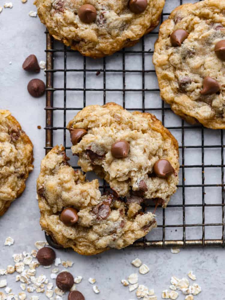 These oatmeal chocolate chip cookies are crispy on the outside, chewy on the inside, and loaded with chocolate! They are insanely delicious, and the flavors combine to make the best cookie of all time! A close up of a oatmeal chocolate chip cookie on a cooling rack, broken in half.