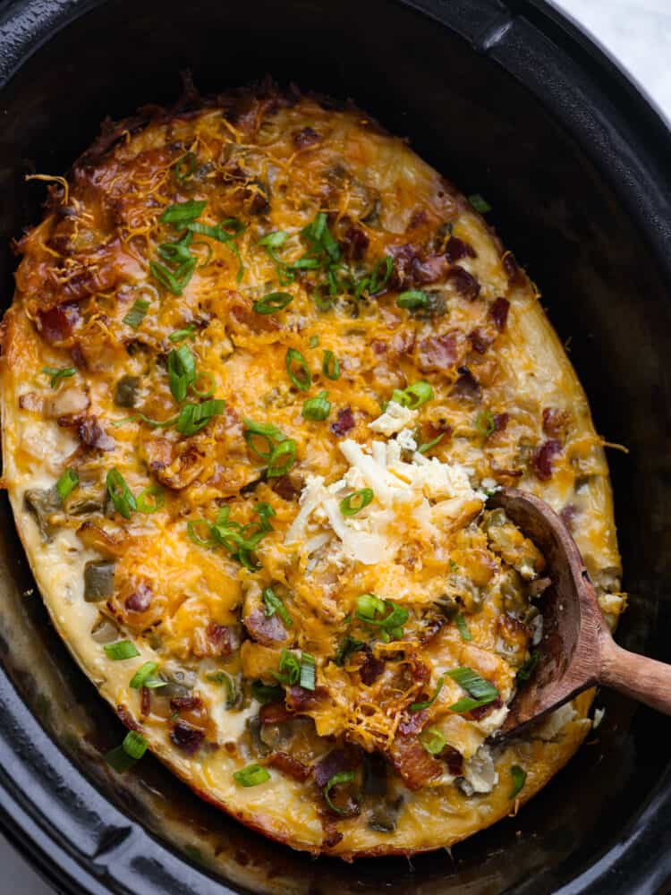 Breakfast casserole in a crock pot with a wooden spoon scoping some out.