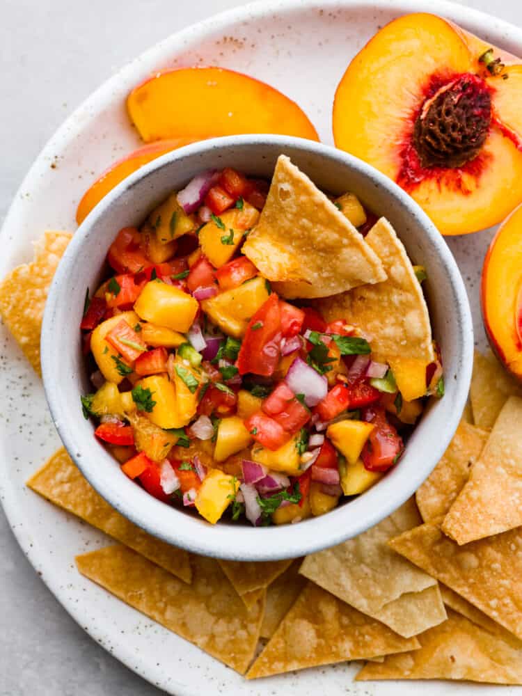 Fresh peach salsa is sweet and savory and the best of both worlds! Vine ripe peaches combined with garden vegetables create a delicious salsa to enjoy with tortilla chips or on chicken or fish. The top view of a bowl of peach salsa with tortilla chips.