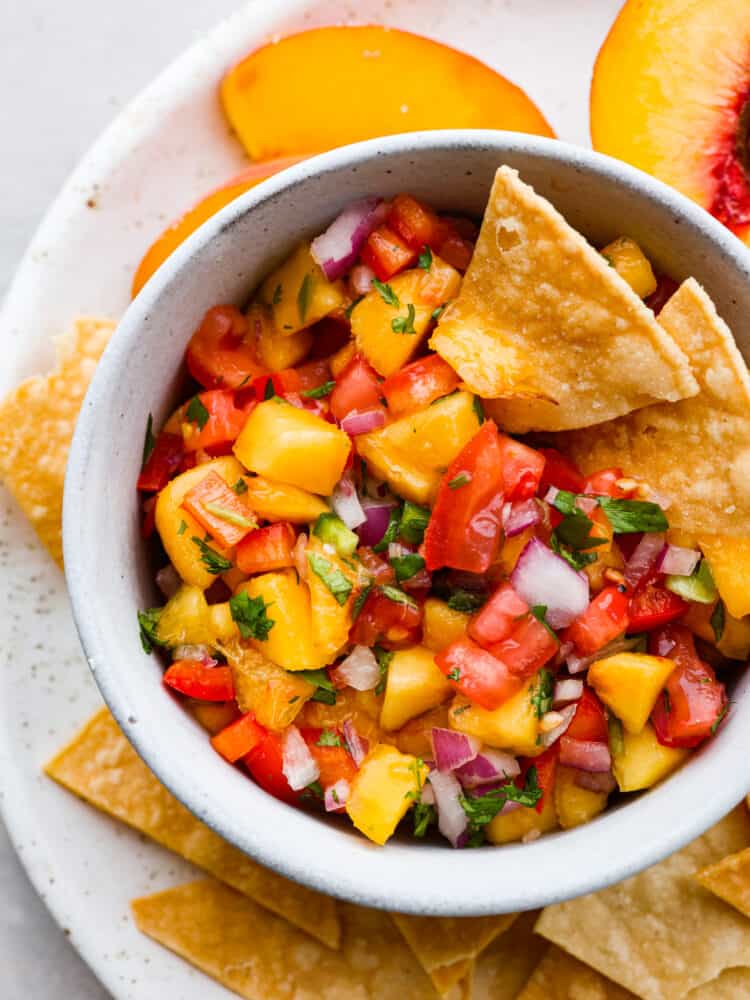 Fresh peach salsa is sweet and savory and the best of both worlds! Vine ripe peaches combined with garden vegetables create a delicious salsa to enjoy with tortilla chips or on chicken or fish. A close up of the top of a bowl filled with peach salsa and tortilla chips.