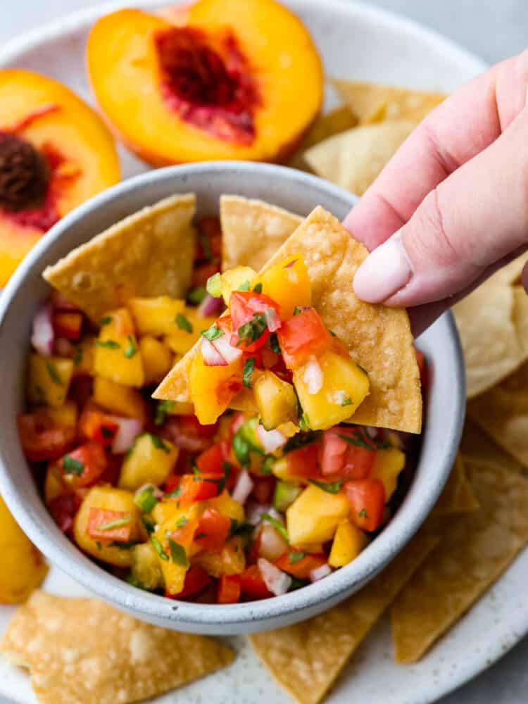 Fresh peach salsa is sweet and savory and the best of both worlds! Vine ripe peaches combined with garden vegetables create a delicious salsa to enjoy with tortilla chips or on chicken or fish. A tortilla chips scooping out peach salsa.