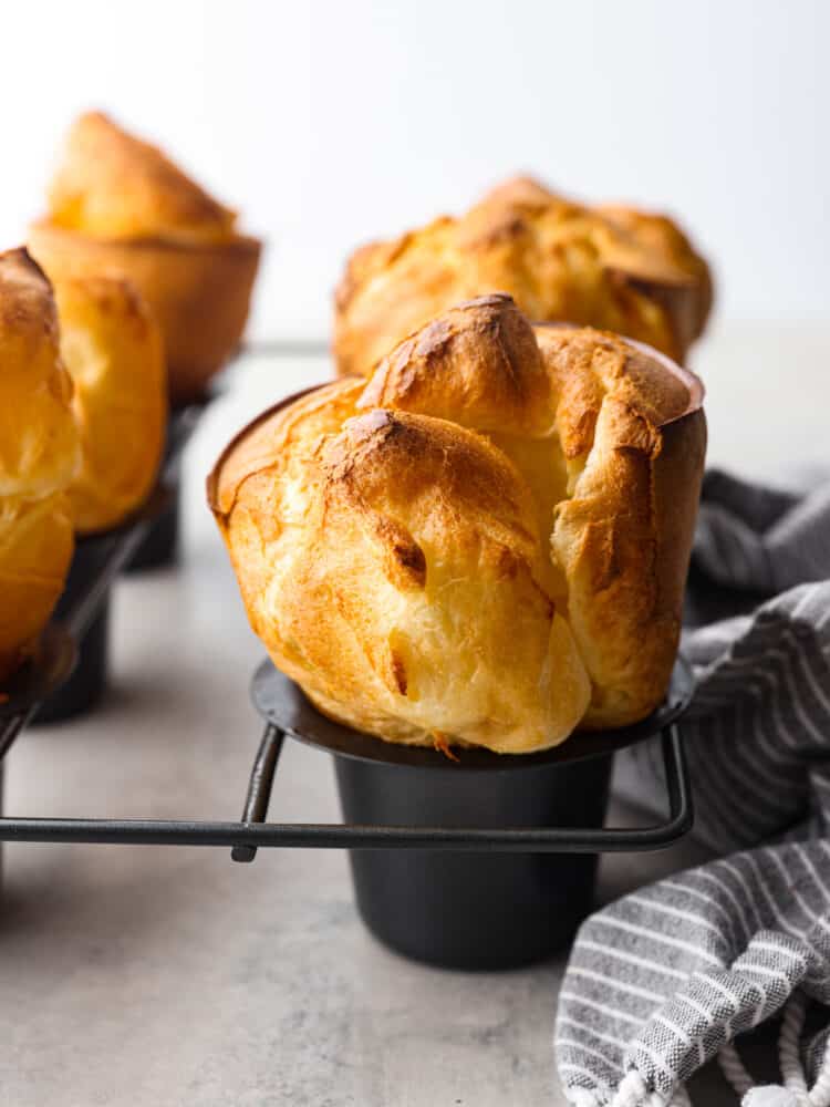 Golden, crisp, and deliciously airy, these homemade popovers are the best addition to any meal! Made with a simple egg batter, popovers have a buttery texture and the perfect chew! Closeup of a baked popover roll, still in the pan.