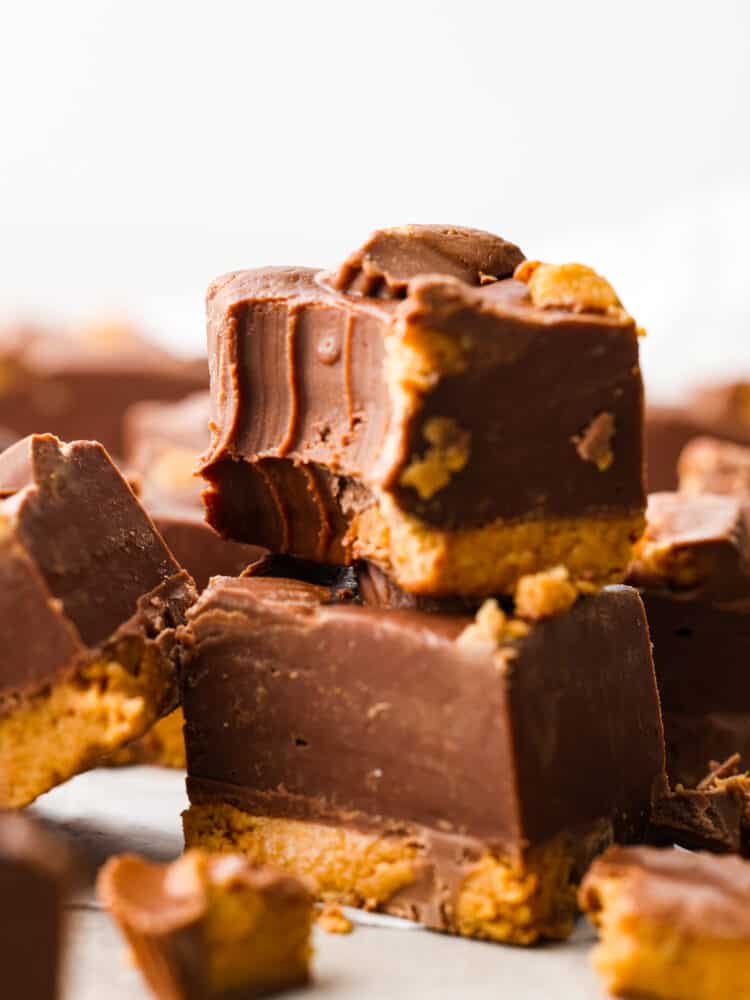 An easy 3 ingredient no-bake fudge that has Reese's Peanut Butter Cups inside. Reeseโs fudge is creamy and delicious and only takes 20 minutes to throw together! It will have the whole family wanting more. Closeup of 2 pieces of fudge stacked on top of each other.