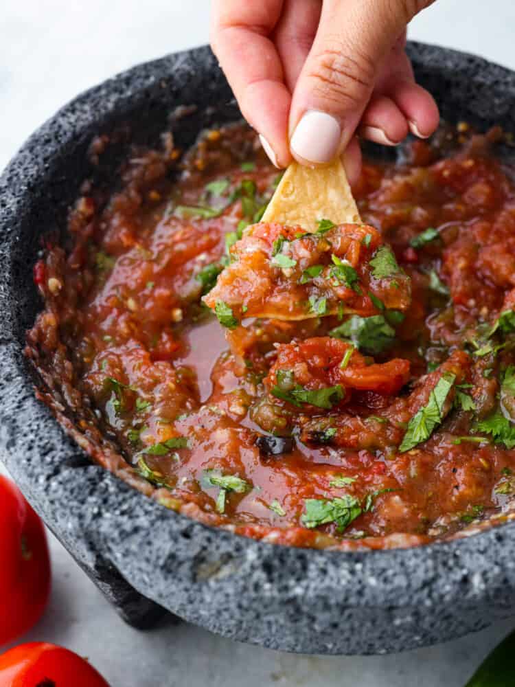 Prepare for the best salsa of your life! This roasted tomato salsa is the best combination of smoky, sweet, and spicy! Youโll be hooked after one dip. Closeup of a chip being dipped in roasted tomato salsa.