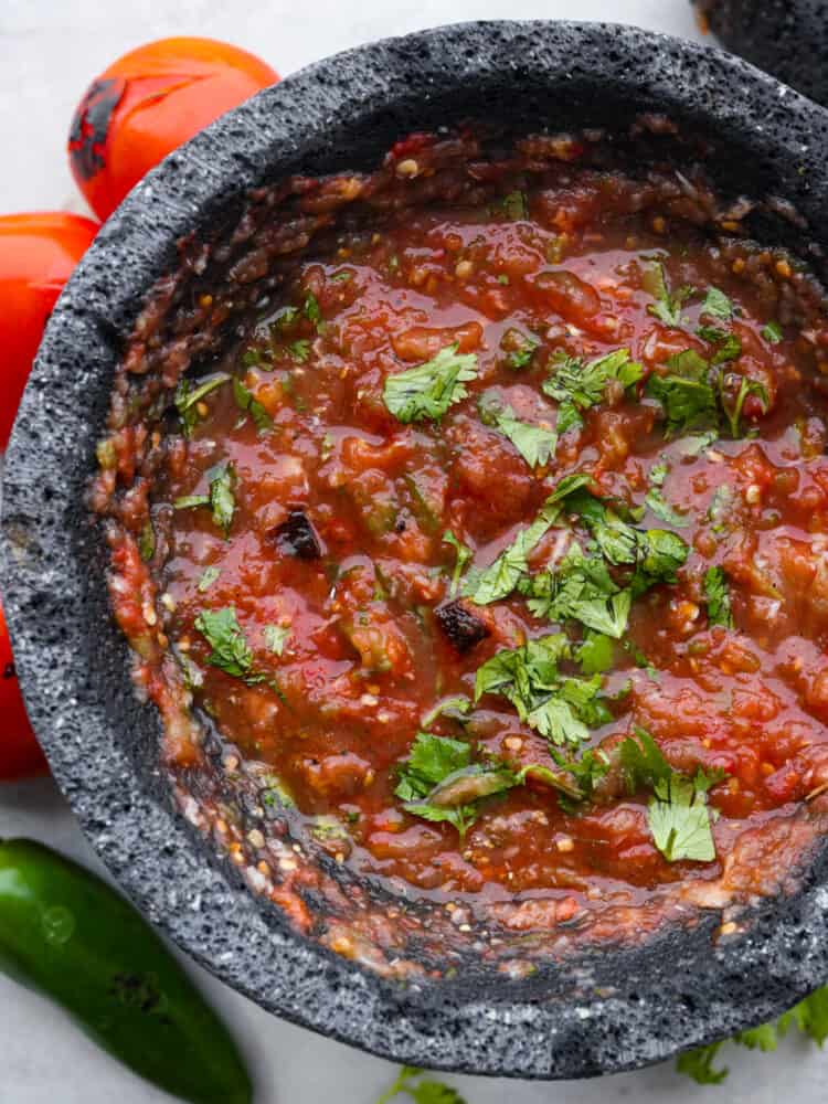 Prepare for the best salsa of your life! This roasted tomato salsa is the best combination of smoky, sweet, and spicy! Youโll be hooked after one dip. Roasted tomato salsa, garnished with chopped cilantro, in a molcajete.