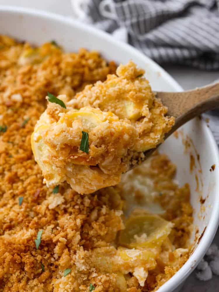 This recipe is the best way to use up that yellow summer squash!ย Squash casserole is a great way to use up fresh squash from your garden. Easy to make with a creamy, cheesy filling and a crispy, buttery topping! Squash casserole being scopped out with a wooden spoon.