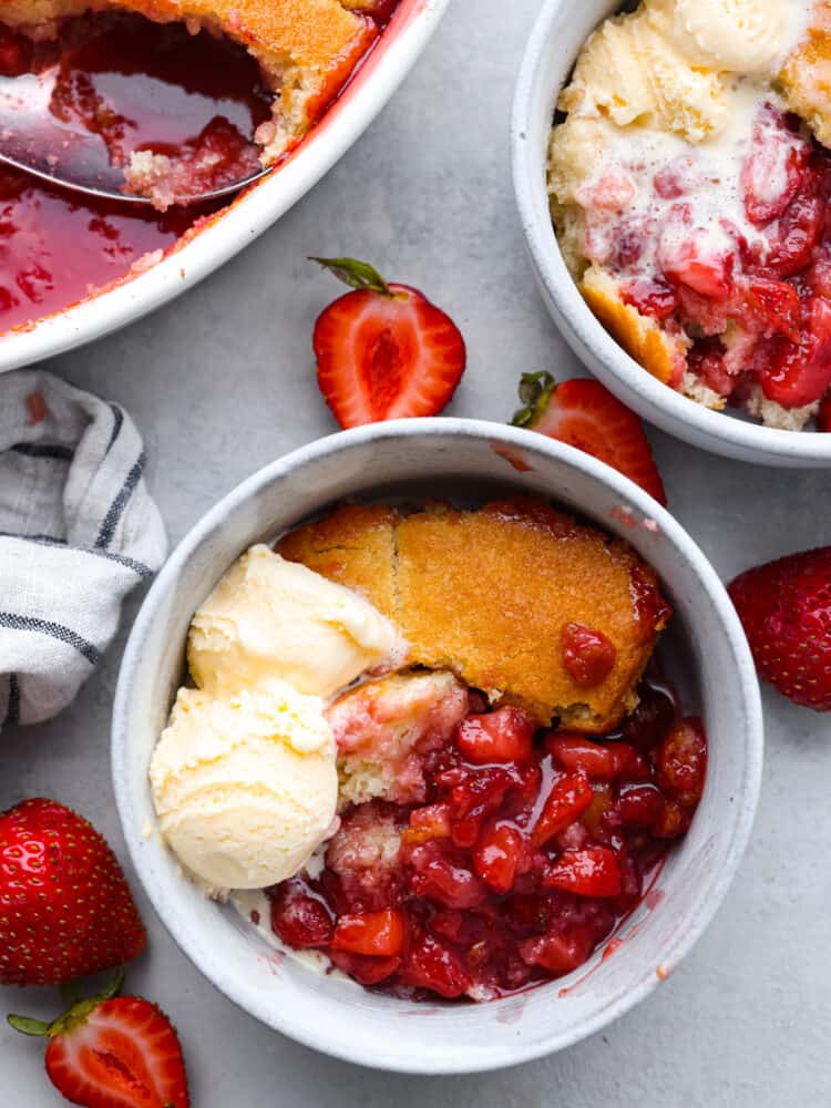 This easy-to-make strawberry cobbler is loaded up with fresh strawberries and topped with a sweet vanilla cake. It's a crisp crust on the outside and is soft and buttery on the inside. Top with some vanilla ice cream for the ultimate treat! The top view of strawberry cobbler in a bowl with a scoop of vanilla ice cream.