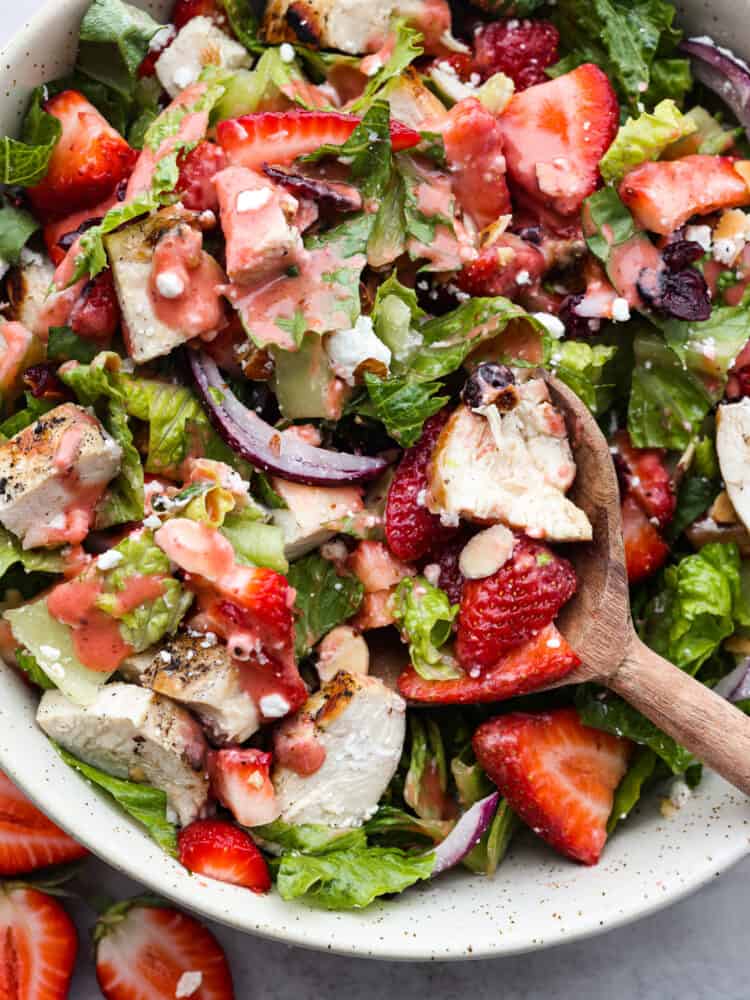 This strawberry chicken salad is filled with fresh fruit, goat cheese, almonds, and chicken and makes my mouth water just thinking about it! The strawberry balsamic dressing gives it the perfect flavor and takes this salad over the top! A close up of strawberry chicken salad with a wooden spoon in the bowl.