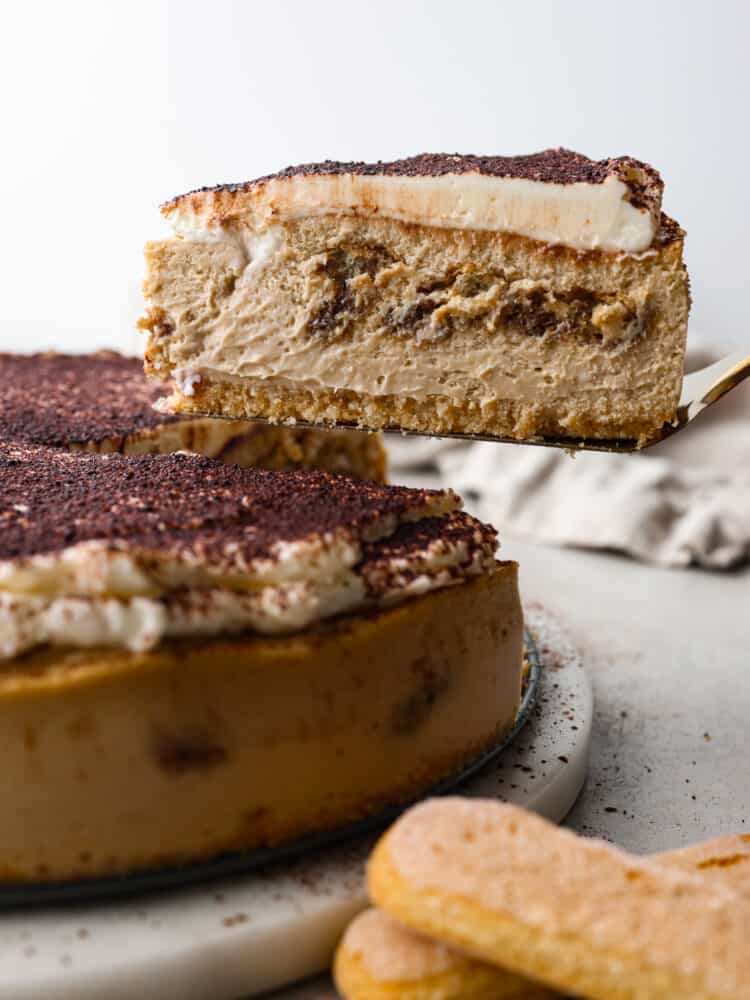 This decadent and delicious tiramisu cheesecake is creamy and will melt in your mouth with every bite. Trust me when I tell you that you will want to make this dessert every time you have guests! The side view of a cheesecake with a slice being taken out.