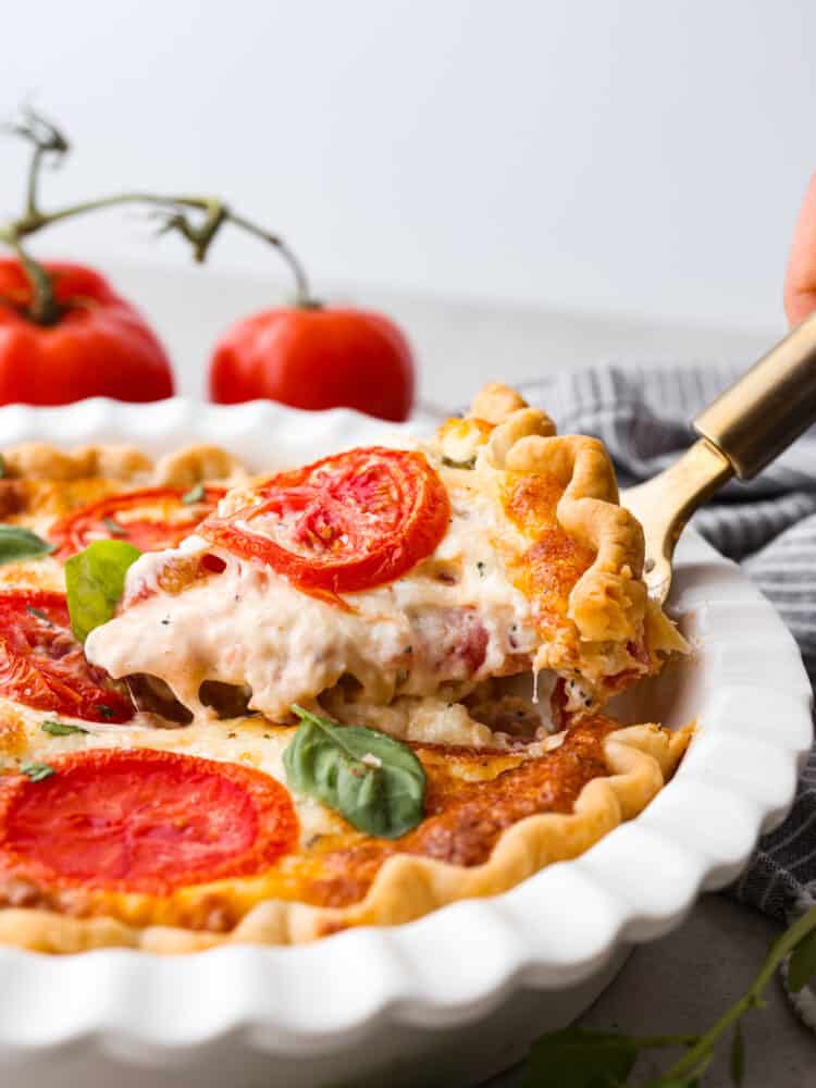 Filled with a cheddar cheese mixture layered in between thick slices of summer tomatoes makes this the best tomato pie. There's no better way to close out summer than making this delicious southern recipe. The side view of a tomato pie with a slice being taken out with a gold pie server.