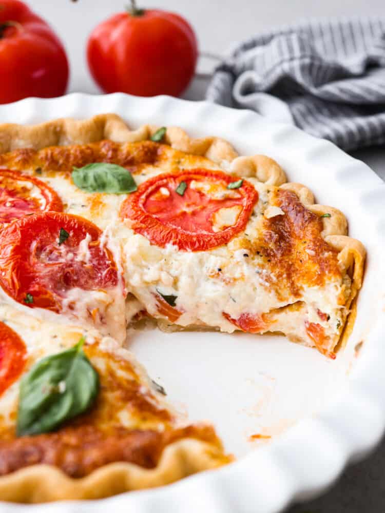 Filled with a cheddar cheese mixture layered in between thick slices of summer tomatoes makes this the best tomato pie. There's no better way to close out summer than making this delicious southern recipe. A tomato pie in a white pie pan with a slice taken out.