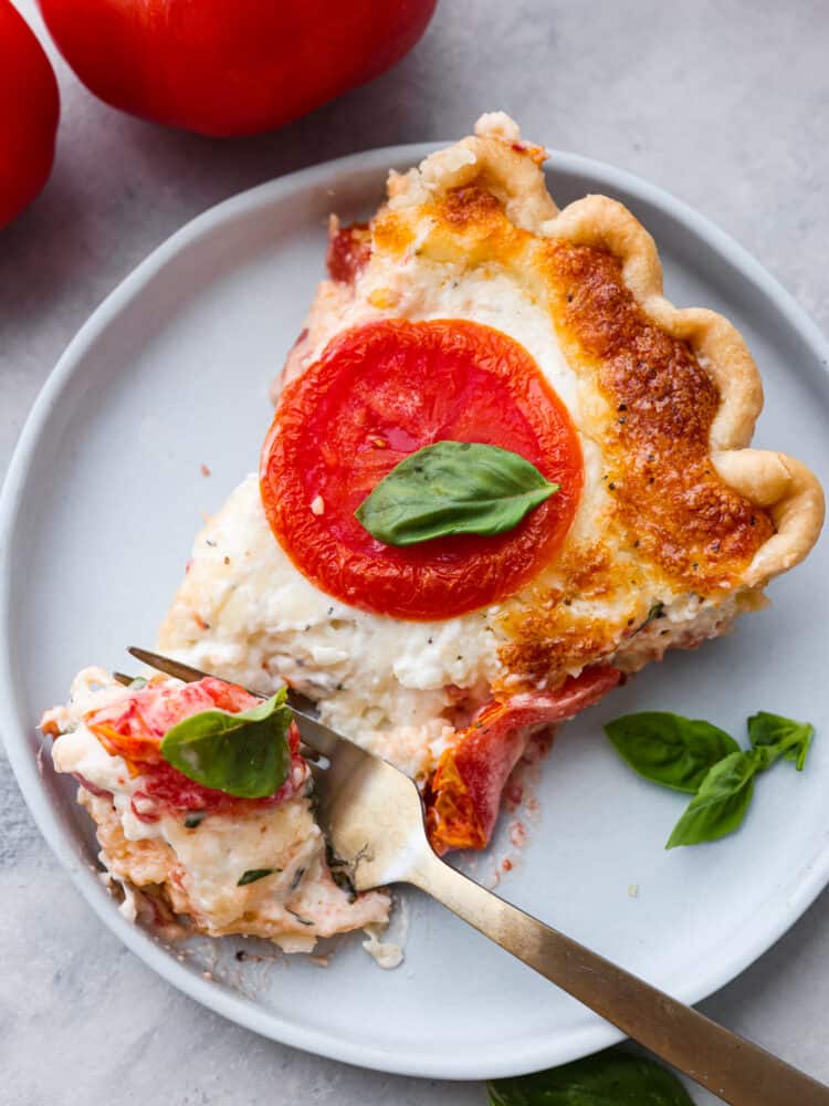 Filled with a cheddar cheese mixture layered in between thick slices of summer tomatoes makes this the best tomato pie. There's no better way to close out summer than making this delicious southern recipe. A slice of tomato pie on a plate with a gold fork.