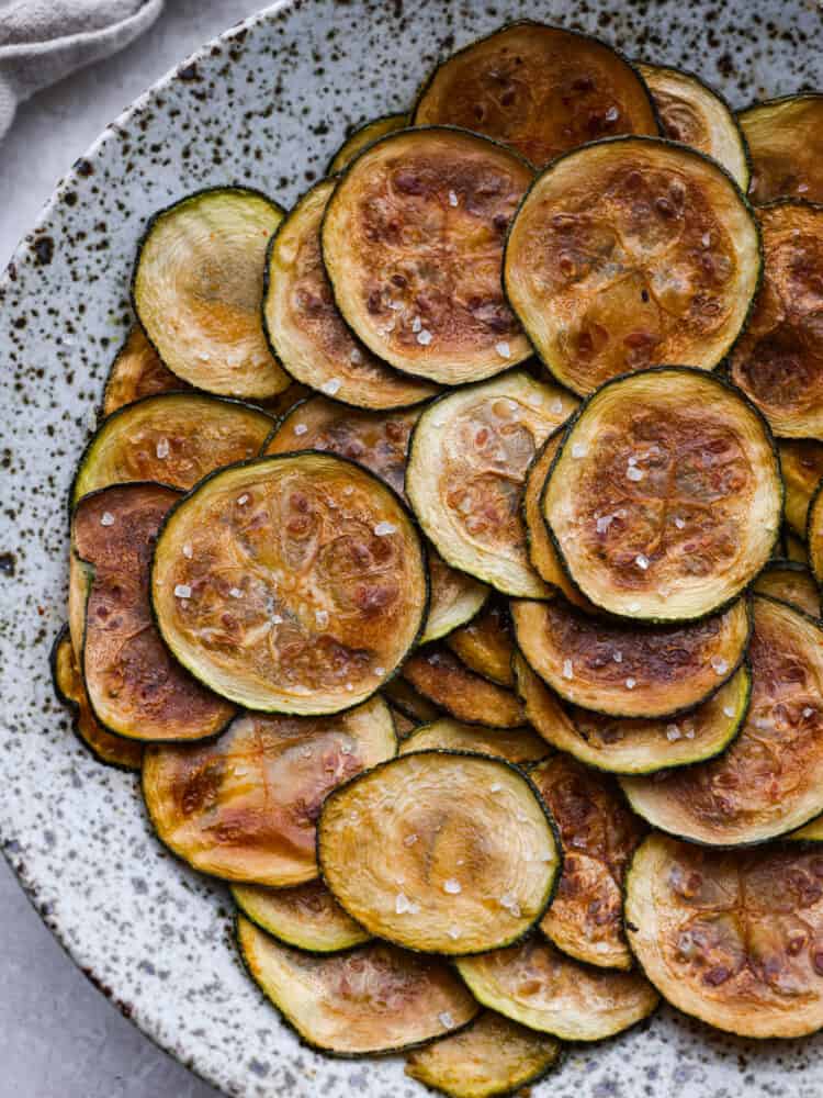 Need something to do with all of that fresh zucchini in your garden? I highly recommend you try this simple recipe for homemadeย zucchini chips! Simple to make and baked in the oven, these are a light, fun snack! Baked zucchini chips on a platter.