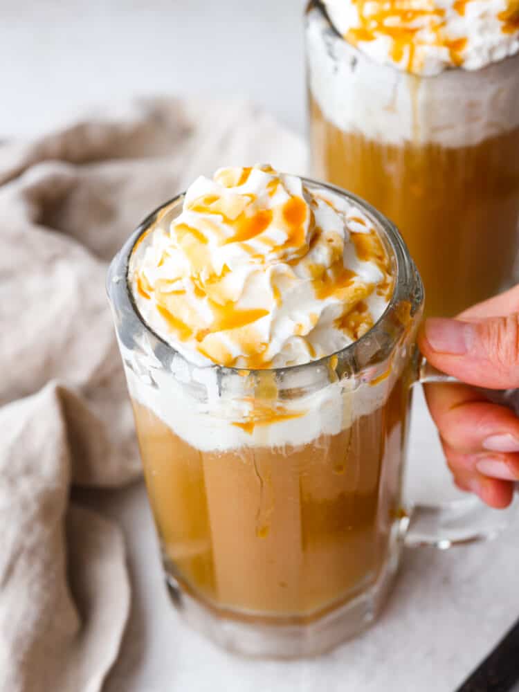 Bring the magic of the wizarding world to your home with a glass of this delectable homemade butter beer! With creamy, butterscotch flavor and whipped cream topping, everyone in your family will be wanting a refill. Closeup shot of butter beer in a glass mug being picked up.