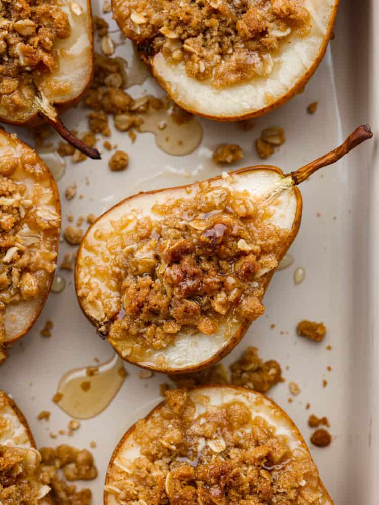 Topped with oats, brown sugar, and cinnamon, these baked pears make the perfect low-calorie cobbler-like treat! Serve them with a side of ice cream for a delicious dessert, or eat them in the morning with some yogurt for a perfectly sweet start to your day. Closeup of a baked pear topped with oats, cinnamon, and brown sugar.