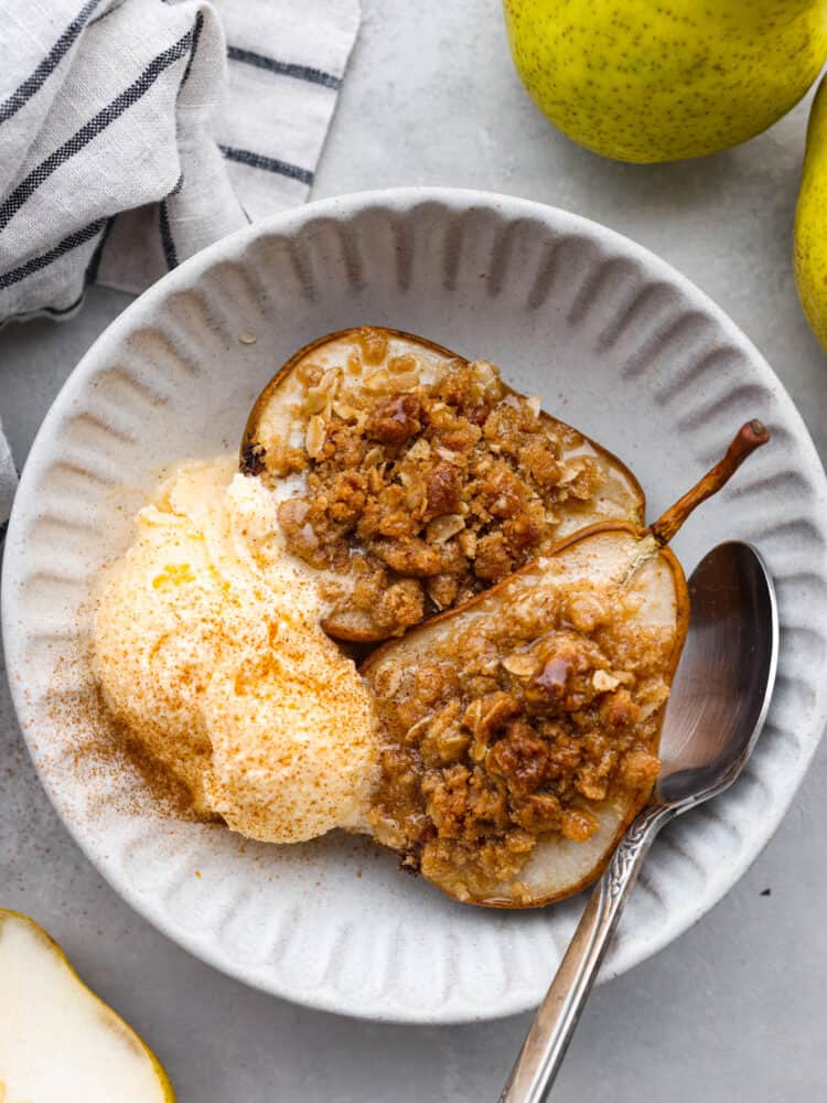 Topped with oats, brown sugar, and cinnamon, these baked pears make the perfect low-calorie cobbler-like treat! Serve them with a side of ice cream for a delicious dessert, or eat them in the morning with some yogurt for a perfectly sweet start to your day. 2 baked pear halves served in a white bowl with a scoop of ice cream.