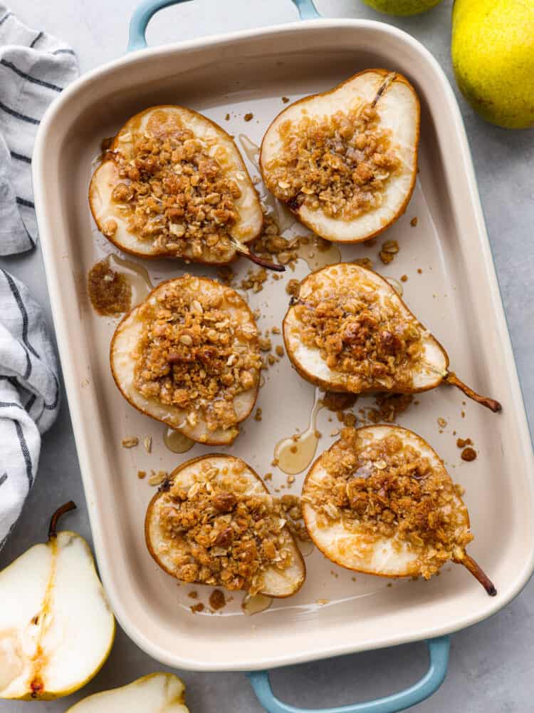 Topped with oats, brown sugar, and cinnamon, these baked pears make the perfect low-calorie cobbler-like treat! Serve them with a side of ice cream for a delicious dessert, or eat them in the morning with some yogurt for a perfectly sweet start to your day. Top-down view of 6 baked pears in a metal baking dish.