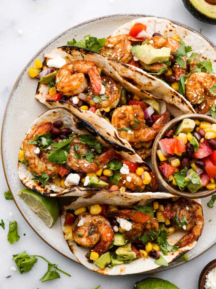 I recommended eating the assembled tacos the same day. If you have leftover shrimp or slaw, you can store in separate air-tight containers in the fridge for up to 2 days. When itโs time to reheat the shrimp, microwave them for about 1 to 2 minutes until they heat through. Or you can place them in a nonstick pan with about a teaspoon of oil and cook for about 1 to 2 minutes until they have heated through. A platter with 4 blackened Cajun shrimp tacos with a small bowl of avocado salsa.