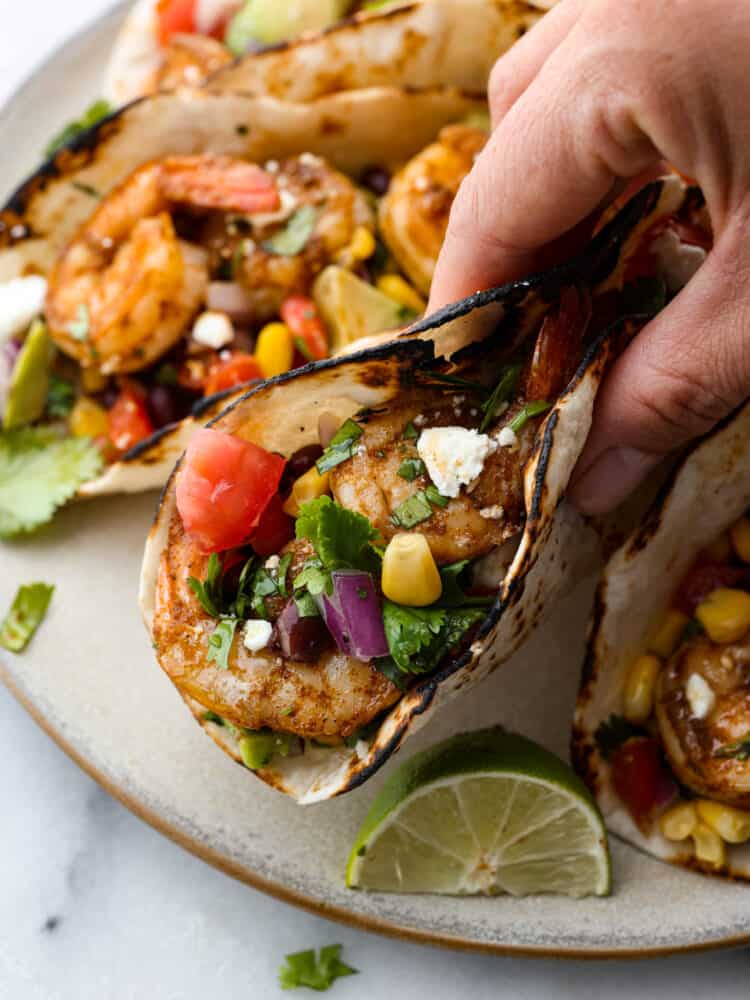 I recommended eating the assembled tacos the same day. If you have leftover shrimp or slaw, you can store in separate air-tight containers in the fridge for up to 2 days. When itโs time to reheat the shrimp, microwave them for about 1 to 2 minutes until they heat through. Or you can place them in a nonstick pan with about a teaspoon of oil and cook for about 1 to 2 minutes until they have heated through. A taco folded in half being held by a hand, about ready to eat.