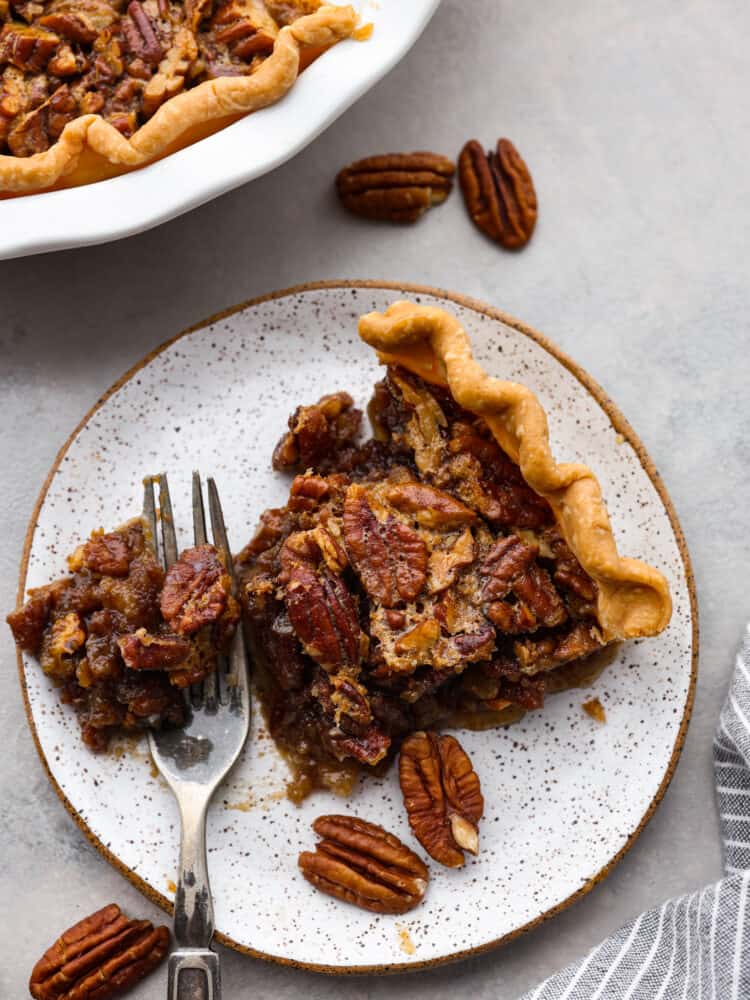 This gooey Bourbon Pecan Pie is a delicious twist on a classic! The alcohol will cook out while baking and you are left with rich flavor and a sweet filling that will leave your mouth watering. You won't want to make it any other way! A slice of pecan pie with a bite taken out sitting on a fork on a stone like plate with the rest of the pie to the side.