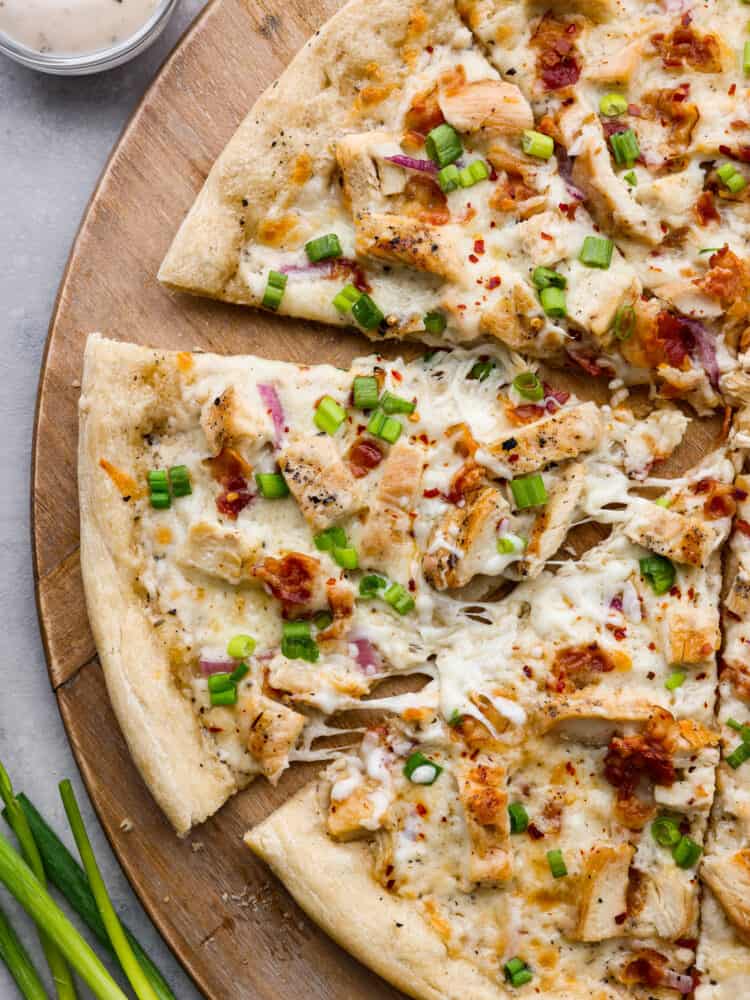 A total win for pizza night, this chicken alfredo pizza will be the best that you make. The homemade alfredo sauce is out of this worldย and the dough is quick and easy with only 20 minutes of rest time! Top-down view of sliced alfredo pizza on a wooden board.