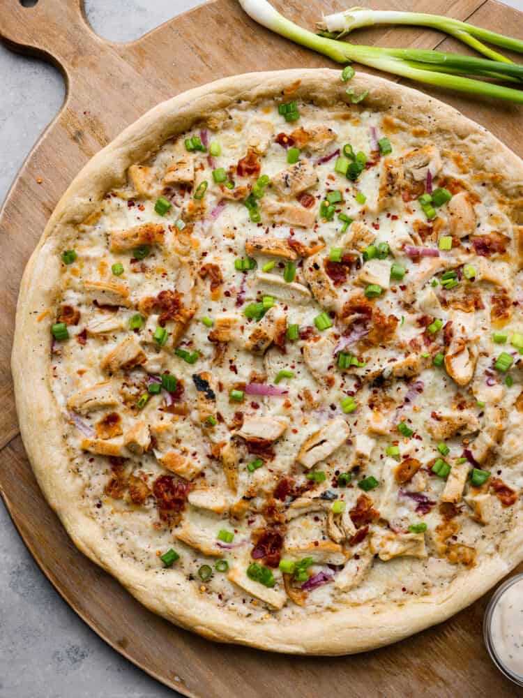 A total win for pizza night, this chicken alfredo pizza will be the best that you make. The homemade alfredo sauce is out of this worldย and the dough is quick and easy with only 20 minutes of rest time! A whole chicken alfredo pizza on a wooden serving board.