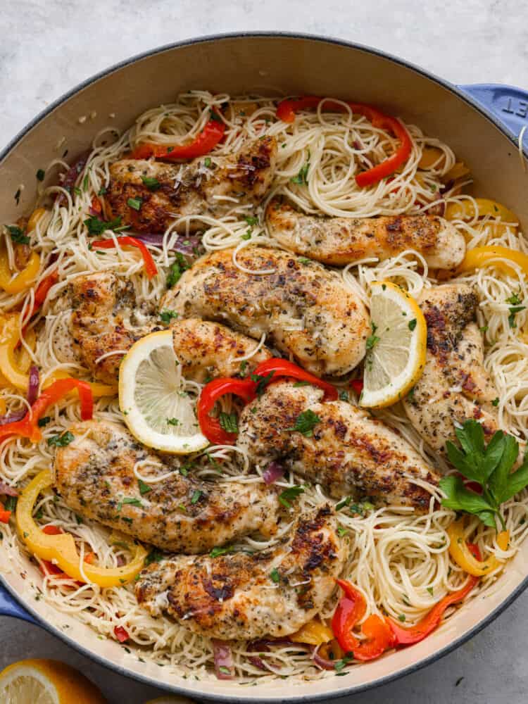 Crispy breaded chicken, angel hair pasta, and an amazing lemon garlic butter sauce combine to make this knockout chicken scampi. It's light, flavorful, and ready in less than 30 minutes! Top-down view of breaded chicken, angel hair pasta, and chopped veggies in a white skillet, garnished with lemon.