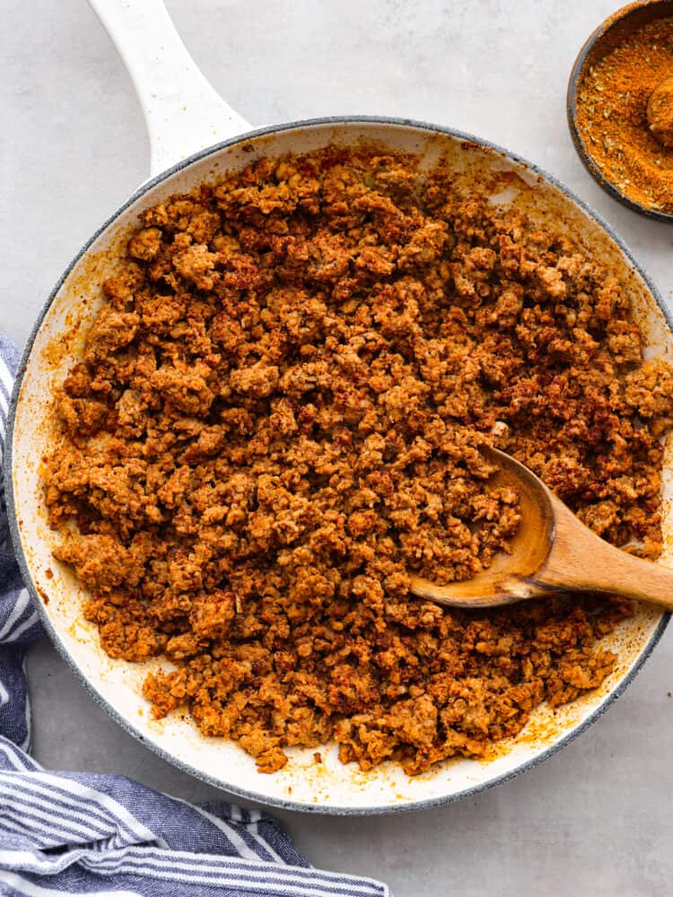 This homemade Mexican chorizo recipe is easy to make and use in any recipe that calls for chorizo meat. Perfectly seasoned ground pork results in the classic flavors of chorizo using authentic spices and a hint of vinegar. You will fall in love with these flavors! Chorizo ground pork in a white pan with a wooden spoon taking a scoop out.