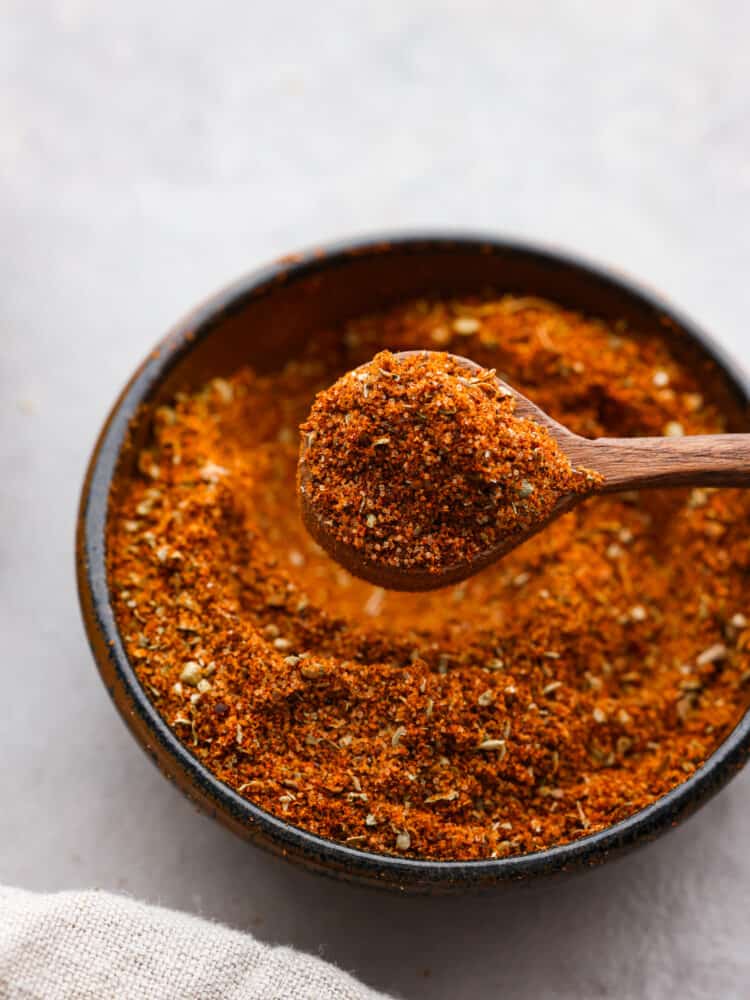 This tasty chorizo seasoning blend is so quick and easy to make but will add the BEST flavor to all of your favorite meat dishes! From sausage to veggies, you're going to love having this warm and savory blend of herbs and spices to use for homemade Mexican dishes! Closeup of chorizo seasoning blend in a black bowl, being scooped up with a small wooden spoon.