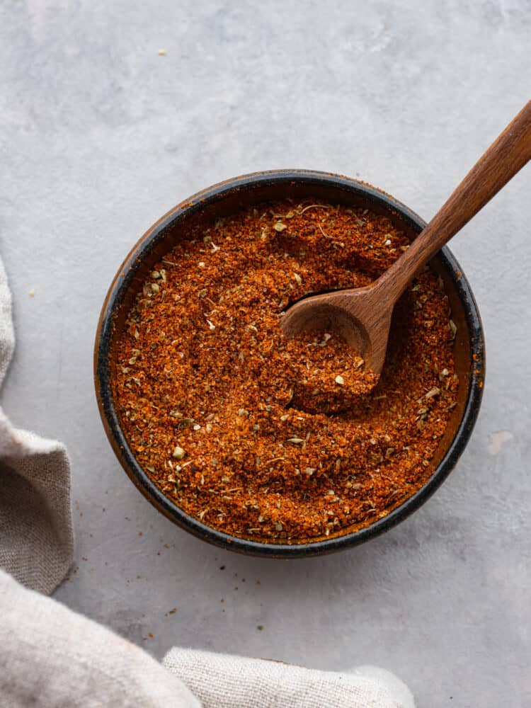 This tasty chorizo seasoning blend is so quick and easy to make but will add the BEST flavor to all of your favorite meat dishes! From sausage to veggies, you're going to love having this warm and savory blend of herbs and spices to use for homemade Mexican dishes! Top-down view of chorizo seasoning blend in a black bowl. There is a wooden spoon in it.