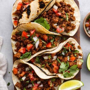Five tacos sitting on a cutting board with limes next to them