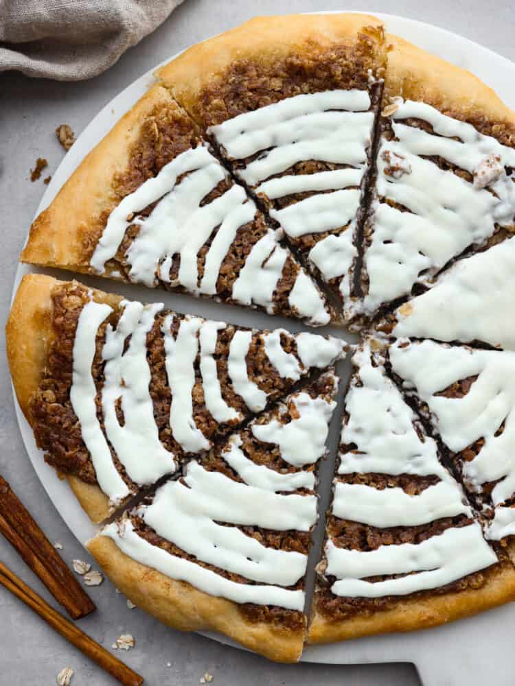 Inspired by Papa Murphy's cinnamon pizza, this dessert pizza has all of the goodness of a cinnamon roll! Buttery brown sugar cinnamon spread on top of quick and easy pizza dough and drizzled with a cream cheese glaze will make you go back for seconds! The top view of a dessert pizza, drizzled with cream cheese frosting and cut into slices on a platter.