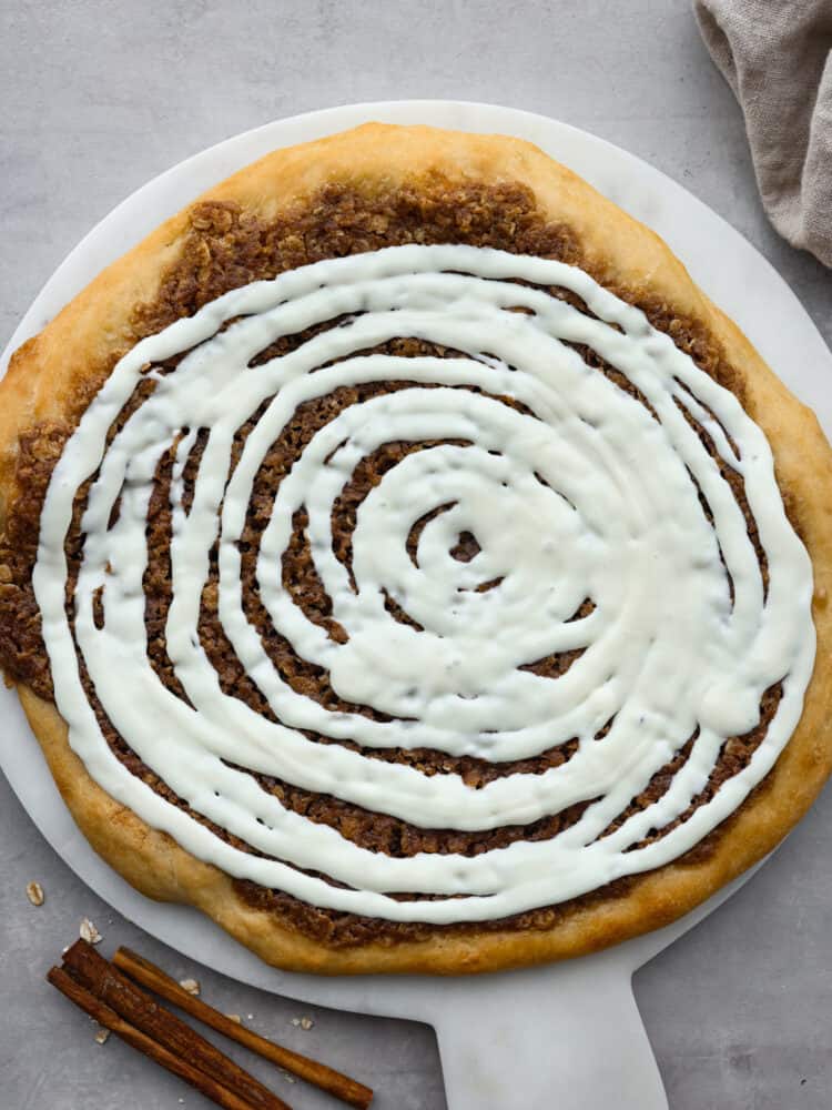 Inspired by Papa Murphy's cinnamon pizza, this dessert pizza has all of the goodness of a cinnamon roll! Buttery brown sugar cinnamon spread on top of quick and easy pizza dough and drizzled with a cream cheese glaze will make you go back for seconds! The top view of a cinnamon roll dessert pizza.
