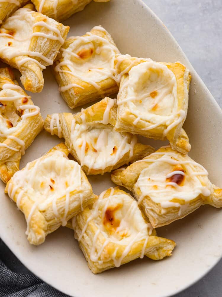 These cheese danishes are flaky, buttery, and full of tangy flavor. Topped with a sweet glaze and baked to perfection, this cheese danish recipe will make the perfect breakfast or dessert for any occasion. They were irresistibly good and gone way too fast! Top-down view of cream cheese danishes on a white plate.
