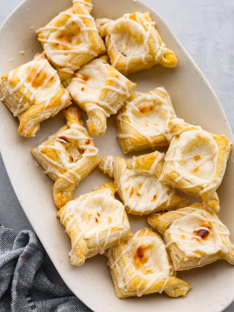 These cheese danishes are flaky, buttery, and full of tangy flavor. Topped with a sweet glaze and baked to perfection, this cheese danish recipe will make the perfect breakfast or dessert for any occasion. They were irresistibly good and gone way too fast! Multiple cheese danishes served on a white plate.